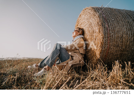 Woman Relaxing by a Hay Bale in a Field Woman Relaxing by a Hay Bale in a Field 136777651