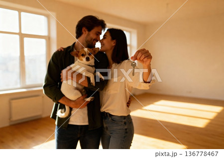Happy young couple with dog holds keys to new home in sunlit room 136778467