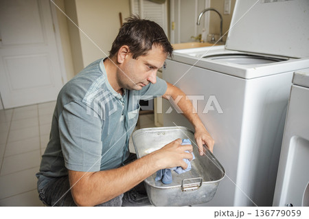 Middle aged man preparing laundry and placing clothes into washing machine at home handling daily household chores in laundry room Middle aged man preparing laundry and placing clothes into washing machine at home handling daily household chores in laundry room 136779059