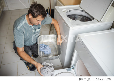 Middle aged man sorting laundry and loading clothes into washing machine at home performing daily household chores in laundry room 136779060