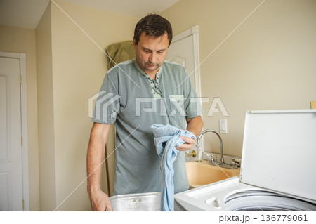 Middle aged man sorting clothes before washing at home preparing laundry for washing machine during daily household routine 136779061