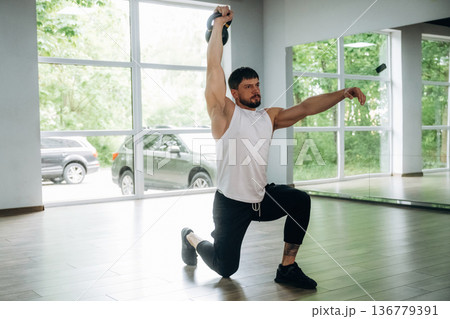 Lifts a kettlebell. Strong man is indoors in the gym with panoramic windows 136779391