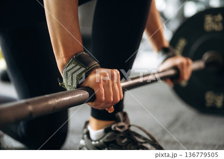 Black weights on the barbell. Close-up of woman with barbell in gym Black weights on the barbell. Close-up of woman with barbell in gym 136779505
