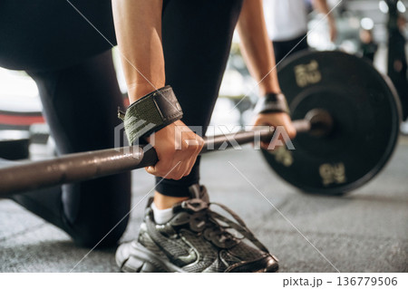 Black weights on the barbell. Close-up of woman with barbell in gym Black weights on the barbell. Close-up of woman with barbell in gym 136779506