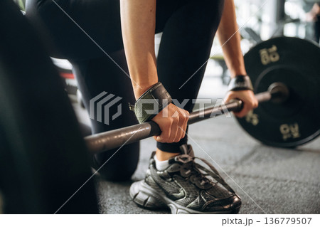 Black weights on the barbell. Close-up of woman with barbell in gym 136779507