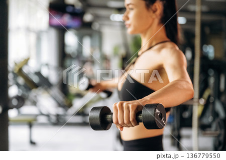 Dumbbells in hands, doing exercise. Beautiful woman is at the gym Dumbbells in hands, doing exercise. Beautiful woman is at the gym 136779550