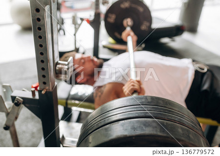 Side view, pushing the barbell. Strong man is working out in the gym 136779572