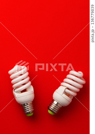 Two spiral light bulbs sit on a red background during daylight hours Two spiral light bulbs sit on a red background during daylight hours 136779839