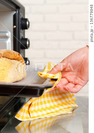 Baker reaches for baked bread from the oven in a kitchen with bright tiles 136779848