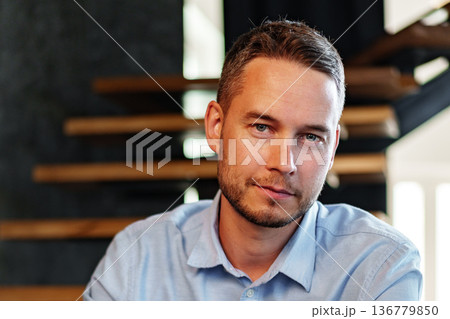 Man poses for a portrait indoors near wooden stair structure during a sunny day 136779850