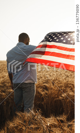 Person holds American flag in wheat field during golden hour 136779890