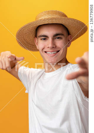 Young man in a straw hat poses with a smile in front of a yellow background Young man in a straw hat poses with a smile in front of a yellow background 136779908
