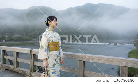 霧の立ち込める嵐山の渡月橋に立つ浴衣姿の日本人女性 136780180