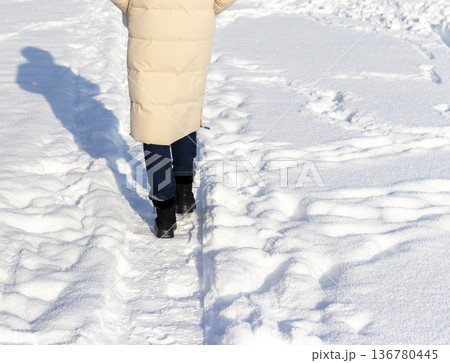 Woman walks outdoor in a winter, wearing beige puffer coat with a hood, snowdrifts all around Woman walks outdoor in a winter, wearing beige puffer coat with a hood, snowdrifts all around 136780445