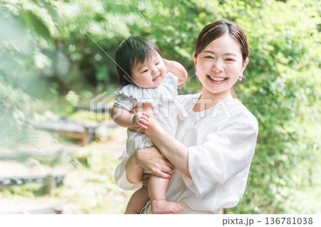 新緑の中で赤ちゃんを抱っこする笑顔の母親 136781038
