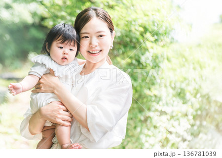 新緑の中で赤ちゃんを抱っこする笑顔の母親 136781039