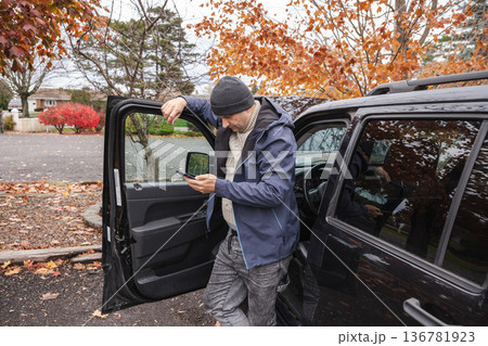 Man standing by open car door and checking smartphone outdoors in autumn Man standing by open car door and checking smartphone outdoors in autumn 136781923