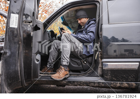 Man sitting in pickup truck and using smartphone during outdoor workday 136781924