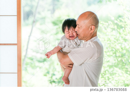 孫がなつかずに悪戦苦闘する赤ちゃんを抱っこするおじいちゃん 136783088