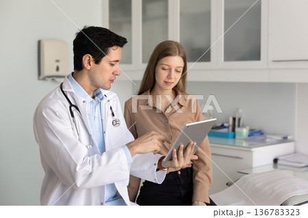 Male physician explains medical information to patient using tablet 136783323