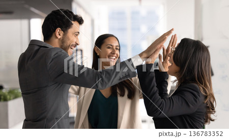 Three multinational happy teammates celebrate joint success in corporate office Three multinational happy teammates celebrate joint success in corporate office 136783352