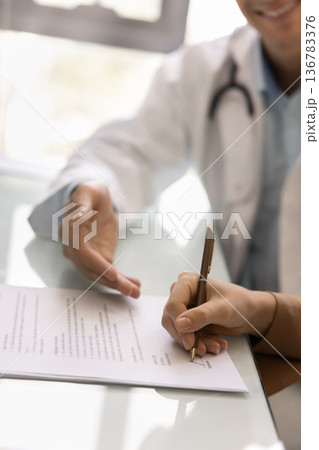 Doctor sitting at desk with patient signing medical documents, closeup Doctor sitting at desk with patient signing medical documents, closeup 136783376