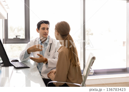 Male doctor and female patient talking seated at desk 136783423
