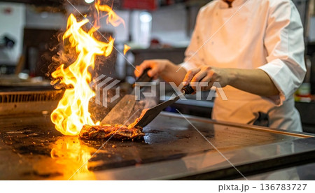 A skilled chef works over the intense heat of a kitchen forge, preparing meat over a burning coal flame where the craft of a blacksmith meets the industry of a professional grill A skilled chef works over the intense heat of a kitchen forge, preparing meat over a burning coal flame where the craft of a blacksmith meets the industry of a professional grill 136783727