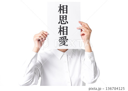 相思相愛と書かれた紙を両手で持つ白いシャツを着た人物 136784125