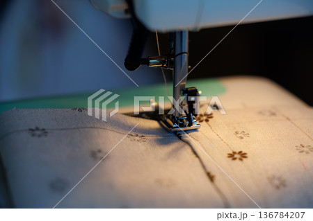Creative sewing session with a sewing machine focused on a delicate patterned fabric in the evening light Creative sewing session with a sewing machine focused on a delicate patterned fabric in the evening light 136784207