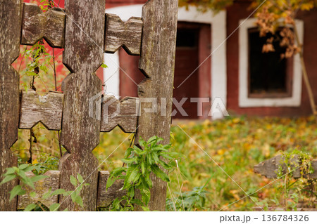 Faded wooden fence with intricate design framing a rustic building in autumn colors at sunset Faded wooden fence with intricate design framing a rustic building in autumn colors at sunset 136784326