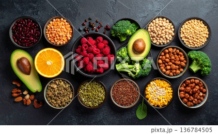 A colorful collection of fresh Easter eggs sits on a rustic wooden background alongside healthy seeds and dried berries in a vibrant display of color 136784505