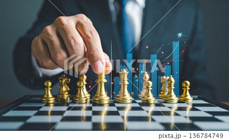 A successful businessman holding a trophy and a growth graph leads his team to checkmate in a strategic battle on the chessboard 136784749