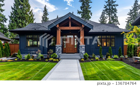 A new luxury residential estate features modern architecture with brick exterior and large windows nestled between a lush green garden lawn and a suburban wooded hill under a clear sky 136784764