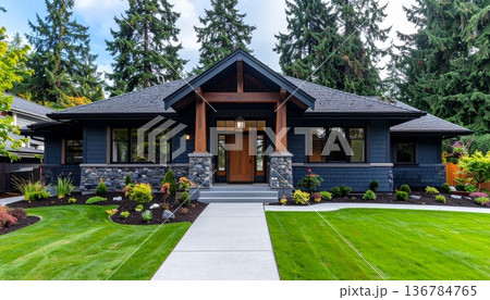 A new luxury residential estate features modern architecture with brick exterior and large windows nestled between a lush green garden lawn and a suburban wooded hill under a clear sky 136784765