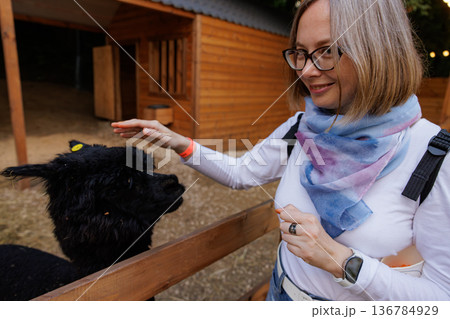 Joyful interaction between a woman and a black alpaca at a cozy farm during a sunny afternoon 136784929