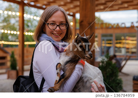 Young woman joyful with a goat in a cozy farm setting during a sunny day Young woman joyful with a goat in a cozy farm setting during a sunny day 136784959
