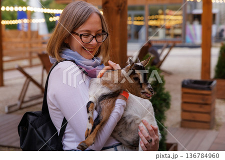 Joyful moment as a woman embraces a goat at an outdoor gathering in the evening light Joyful moment as a woman embraces a goat at an outdoor gathering in the evening light 136784960
