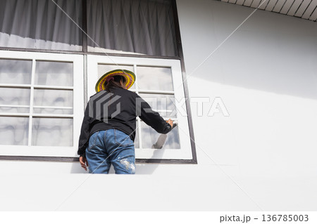 Woman painting exterior window frame of a house during home renovation. Woman painting exterior window frame of a house during home renovation. 136785003