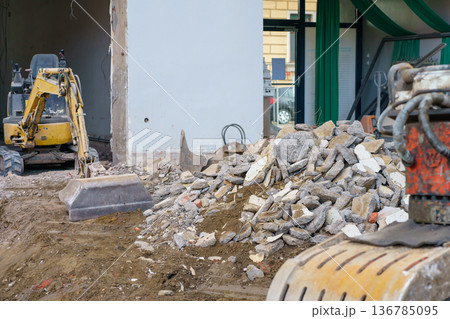 Pile of concrete rubble in foreground and excavator in background during demolition and reconstruction of urban property. 136785095