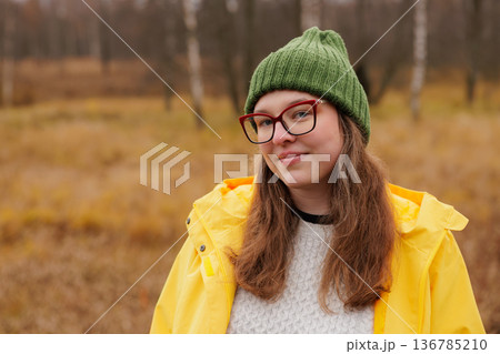 Bright yellow raincoat worn by a cheerful young woman in a serene autumn landscape Bright yellow raincoat worn by a cheerful young woman in a serene autumn landscape 136785210
