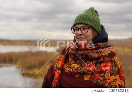 Captivating autumn moment by the tranquil lake with a young woman wrapped in a colorful shawl 136785218