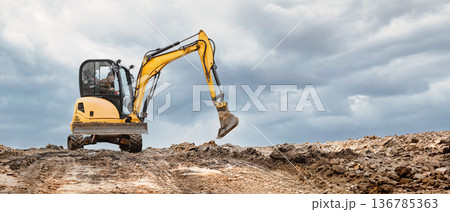 A mini excavator on a hill at a construction site. Compact equipment for challenging construction conditions 136785363