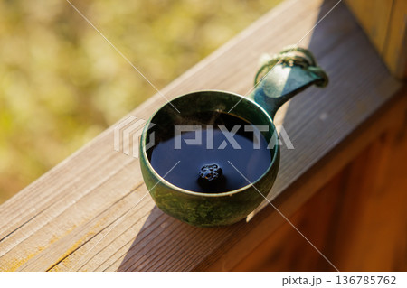 Steaming cup of dark beverage resting on wooden porch in morning light 136785762