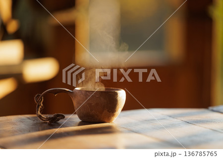 Warm steam rises from a rustic wooden cup in a cozy setting during the golden hour of sunset 136785765