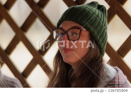 Charming young woman in a cozy green beanie enjoying nature on a crisp autumn afternoon 136785804