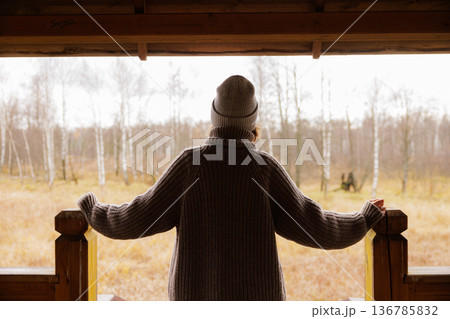 Gentle autumn breeze whispers through birch trees as a figure enjoys quiet solitude on a rustic porch Gentle autumn breeze whispers through birch trees as a figure enjoys quiet solitude on a rustic porch 136785832