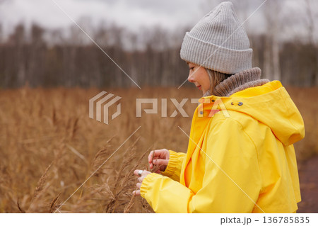 Woman enjoys a peaceful afternoon in a golden field wearing a cozy yellow jacket and gray beanie Woman enjoys a peaceful afternoon in a golden field wearing a cozy yellow jacket and gray beanie 136785835