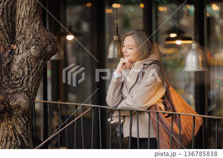 Thoughtful woman enjoying a quiet moment by a cozy cafe in the evening glow of warm lights 136785838