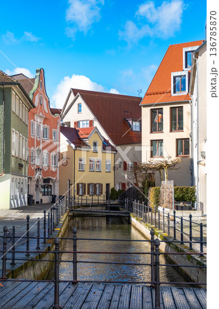 Colourful houses line the streets of Memmingen, Germany, alongside tranquil water canals. A clear blue sky enhances the picturesque scene. Colourful houses line the streets of Memmingen, Germany, alongside tranquil water canals. A clear blue sky enhances the picturesque scene. 136785870